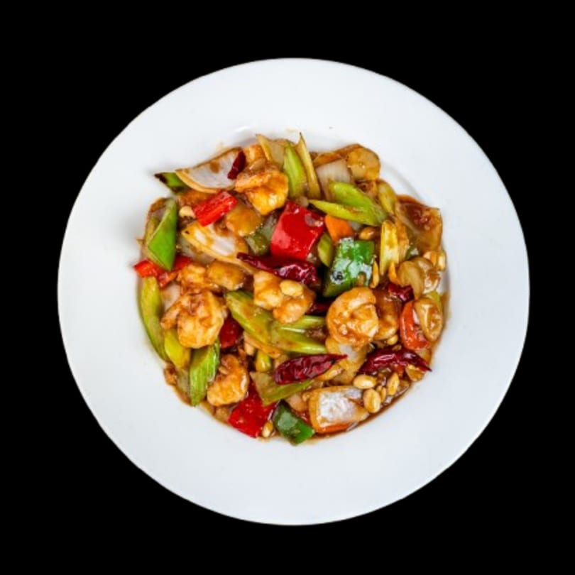 Kung Pao shrimp with peanuts, red and green peppers, and onions on a white plate.