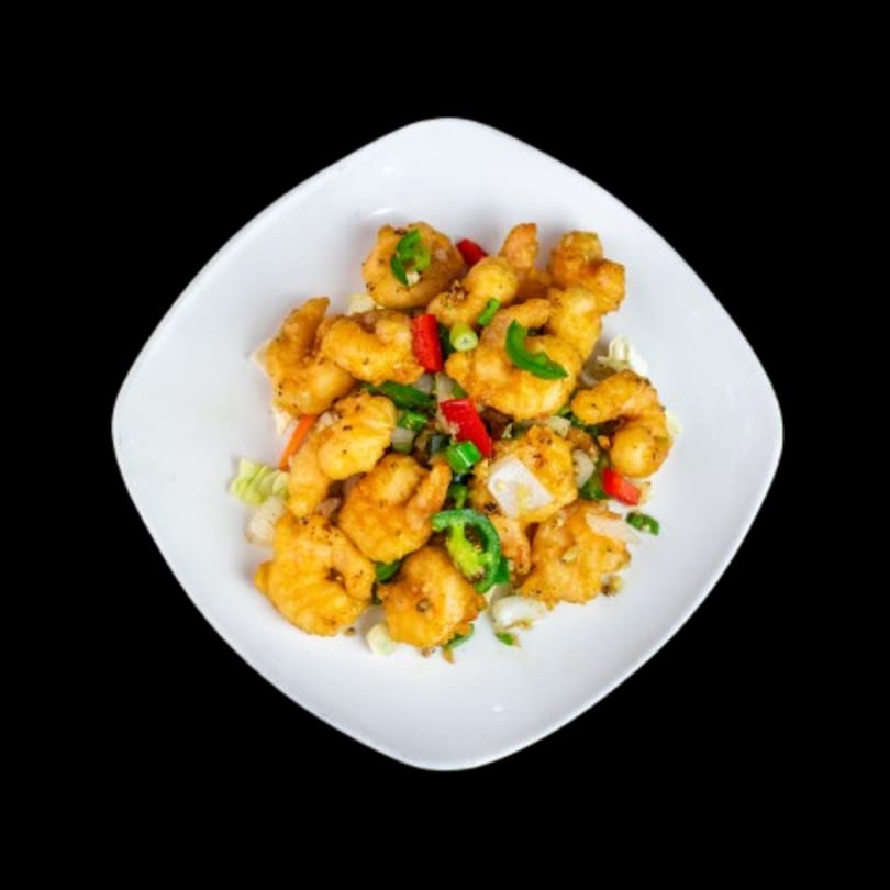 Crispy golden fried shrimp with red and green peppers, onions, and garlic on a white plate.